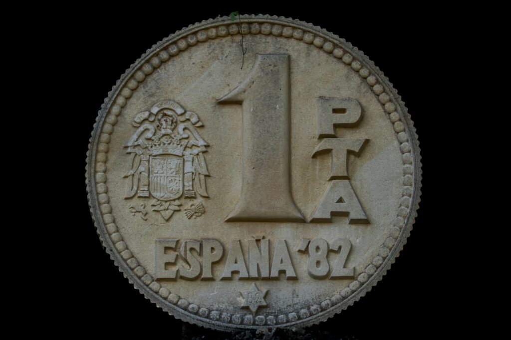 Large stone sculpture of a 1 peseta coin from Spain, 1982, with detailed engravings.