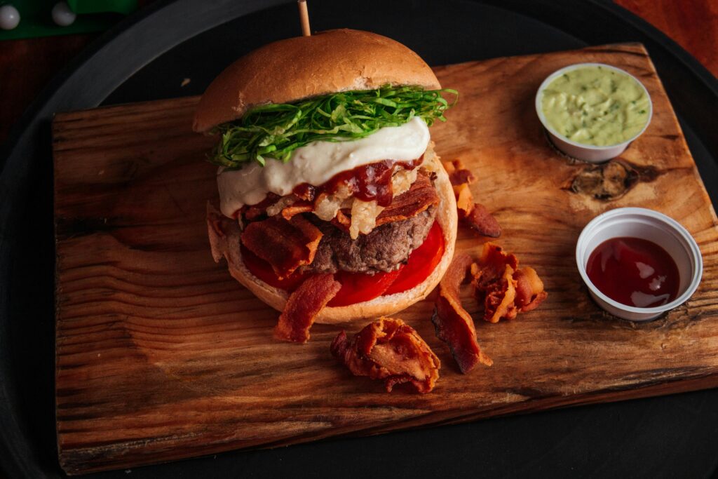 Mouth-watering burger with bacon, fries, and avocado sauce on a wooden board.