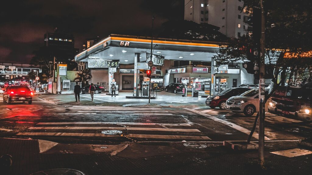 Cars driving down asphalt busy roadway with crossing near modern illuminated gas station
