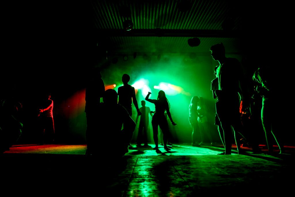 People dancing in a nightclub with colorful green lighting and vibrant atmosphere.