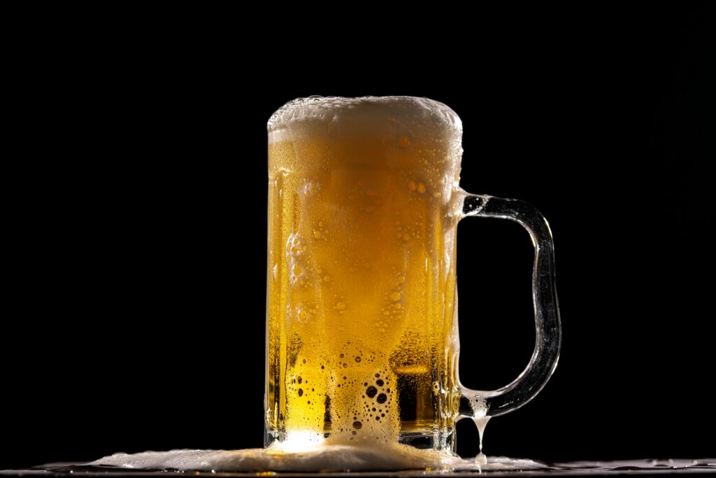 Close-up of a full beer mug with frothy foam on top, beautifully contrasted against a black backdrop.
