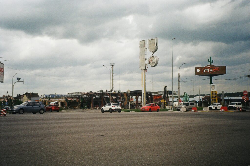 Urban street view in Kyiv showing cars, cloudy sky, and damaged structures.