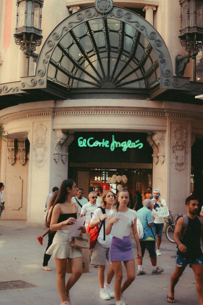 Pedestrians outside the entrance of El Corte Inglés with an ornate facade in an urban setting.