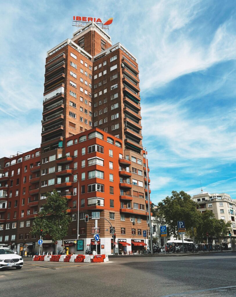 A tall terracotta building featuring an Iberia sign dominates the vibrant urban landscape.