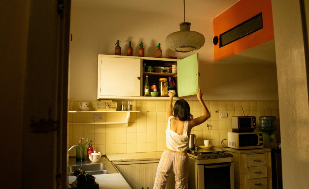 Woman in kitchen reaching for items on a high shelf, cozy home scene.