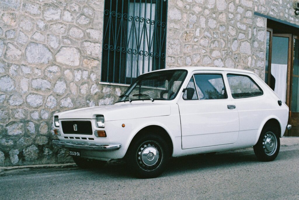 Classic white vintage car parked by a textured stone wall, exuding retro charm.