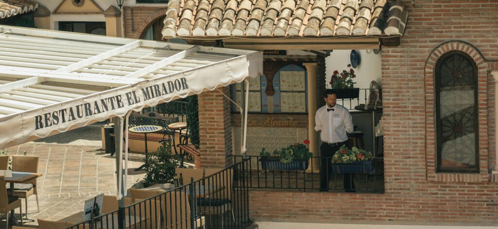 Outdoor view of a traditional Spanish restaurant with a waiter and rustic architecture.