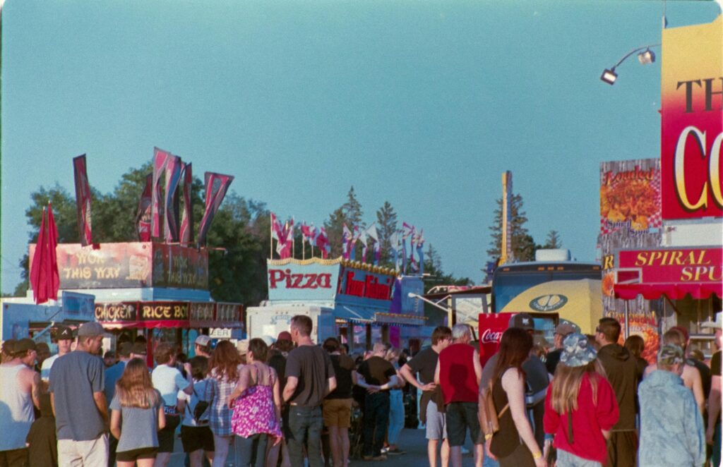 Crowd enjoying a lively outdoor festival in Saskatoon with colorful stalls and clear skies.